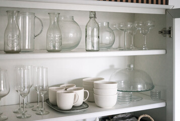 Fototapeta na wymiar White shelves in a cabinet with glass and porcelain utensils