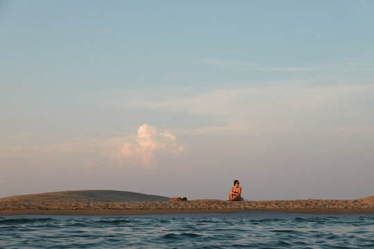 jeune femme assise sur une plage déserte au coucher du soleil dans le sud de la France