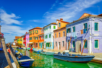 Fototapeta na wymiar Colorful houses of Burano island. Multicolored buildings on fondamenta embankment of narrow water canal with fishing boats and wooden bridge, Venice Province, Veneto Region, Northern Italy