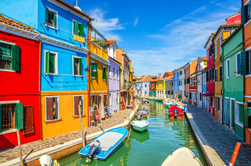 Fototapeta premium Colorful houses of Burano island. Multicolored buildings on fondamenta embankment of narrow water canal with fishing boats in sunny day, Venice Province, Veneto Region, Northern Italy. Burano postcard