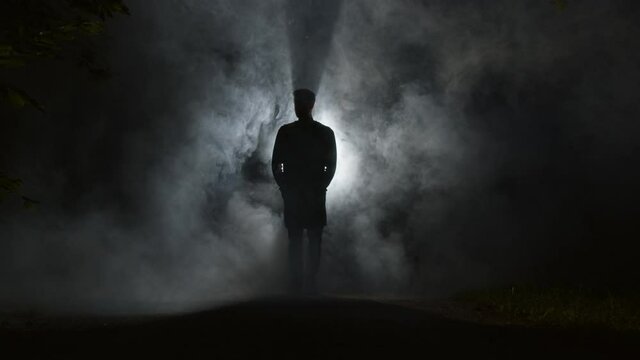 A silhouette of a man is walking through mist