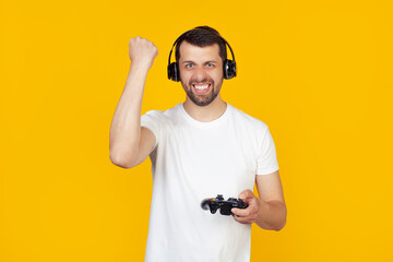Young man with beard in white t-shirt gamer playing video games with headphones annoyed and frustrated screaming with anger, crazy and screaming with raised hand, anger concept. yellow background