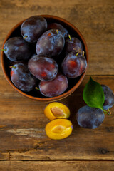 Blue plum in a bowl on a wooden table. Plums in a cut. Top view, place for text. Fruit background with copy space. Still life food.