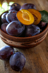 Fototapeta premium Blue plum in a bowl on a wooden table. Plums in a cut. Top view, place for text. Fruit background with copy space. Still life food.