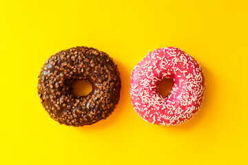 Two donuts on a bright yellow background. Chocolate and strawberry donuts with sprinkles close-up. Flat lay, top view