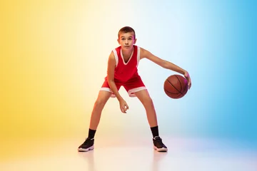  Full length portrait of young basketball player in uniform on gradient studio background. Teenager confident practicing with ball. Concept of sport, movement, healthy lifestyle, ad, action, motion. © master1305