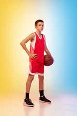 Fototapeta na wymiar Full length portrait of young basketball player in uniform on gradient studio background. Teenager confident posing with ball. Concept of sport, movement, healthy lifestyle, ad, action, motion.