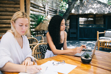 Pensive caucasian women colleagues working remotely during vacation together planning and researching information, serious hipster girl learning outdoors using laptop computer and 4G connection