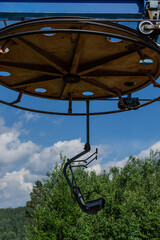 old cable car round circle construction with seat in the forest with green trees, sunny summer blue sky with white clouds