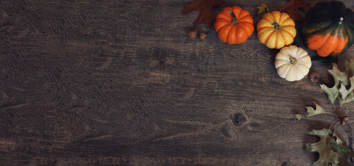 Fall Thanksgiving and Halloween pumpkins, leaves, acorn squash over rustic dark wood table background shot from directly above, horizontal with copy space - Powered by Adobe