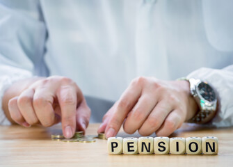 Closeup wooden block written PENSION against senior man hand putting coin into piggy bank to saving money for retirement financial and pension annuity insurance. Concept for loan,property,financial.