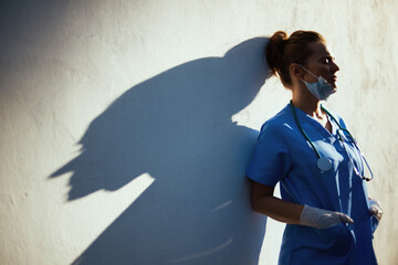 tired modern medical doctor woman outdoors in city near wall