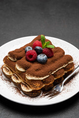 portion of Classic tiramisu dessert with raspberries and blueberries on dark concrete background