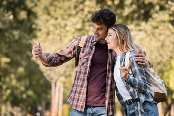 man taking selfie with woman showing peace sign in autumnal park