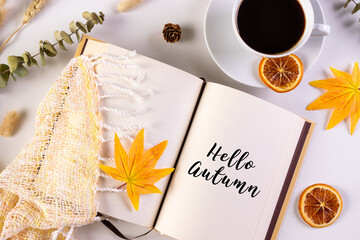 Autumn leaves, cup of coffee, book reading warm scarf and opened book on the table with text Hello Autumn. Fall and autumn concept.