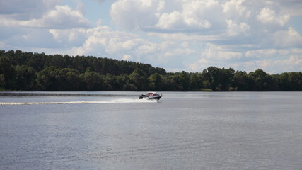Russian river Volga with fast floating motor boat on riverside forest and sky with clouds background, beautiful natural landscape at summer day