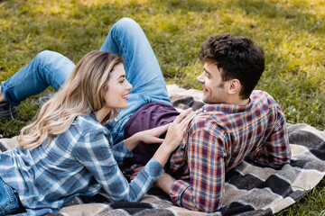 Fototapeta na wymiar woman lying on plaid blanket and touching boyfriend in park