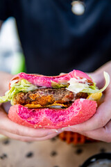 Woman holding a pink beetroot gluten-free hamburger bun with vegan black beans patty, nachos, jalapeño, lettuce and Mexican sauce eaten during lunchtime in a vegan restaurant 
