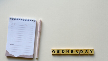 Notepad with pen and wooden word "Wednesday" on a beige paper background. Top view. Close-up. Flat lay.