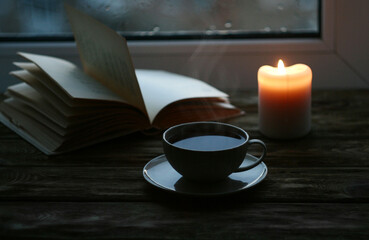 Evening, a cup of hot tea on the table, there is a candle nearby and a book