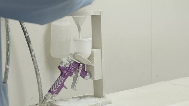 Laborer pours white paint into a airbrush tool preparing to work in a spray booth slow motion