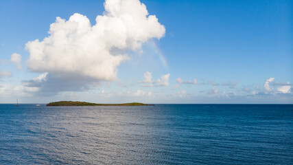 Naklejka na ściany i meble Rainbow over the ocean with island and clouds, drone shot