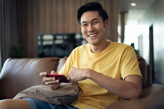 Asian Young Man In Casual Style Clothes Stay At Home And Relaxing With Smartphone On The Sofa.