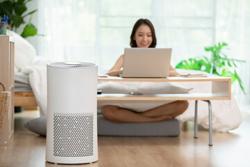 air purifier in living room for clean and fresh air with woman working with computer laptop and...