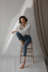 Mid age woman with slim body in a white shirt and blue jeans looking in camera and posing on a...