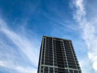 Obraz premium a tall, multi-storey glass building in a white and brown city. the house has balconies, stylish decoration. ergonomic arrangement. against the backdrop of a sunny blue sunny sky