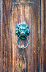 Detail of an ancient wooden door aged by time with a metal lion head shaped door knocker with a ring in the mouth