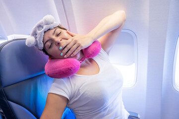 Naklejka premium Woman yawns while sitting on the plane with a mask and a pillow for sleeping.