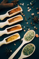 Various spices and herbsin in a wooden spoons on dark stone table. Indian cuisine. Top view.