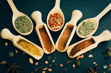 Various spices and herbsin in a wooden spoons on dark stone table. Indian cuisine. Top view. - 379431998