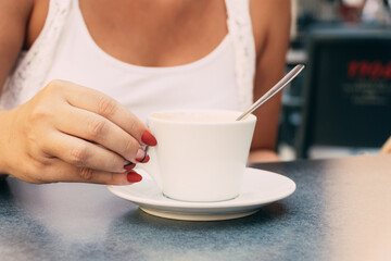 Closeup shot of a woman's hand with a red nail polish holding a white cup
