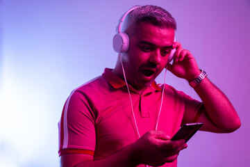 Neon light portrait of stunned man in headphones, red t-shirt.