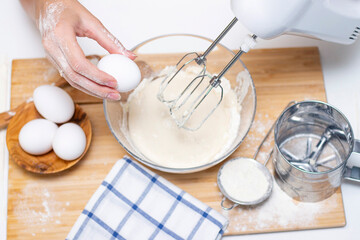 making dough for bread or homemade baked goods. ingredients on the desk. female hands holding an egg