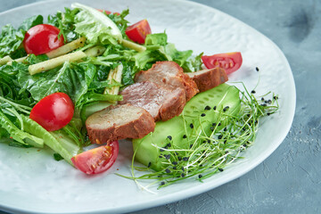Baked pork fillet salad with tomatoes, arugula, leaves in a white plate on a gray background