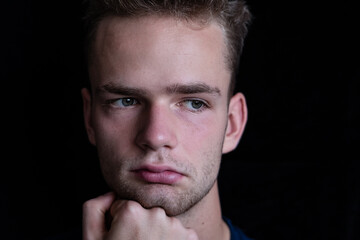 Dramatic portrait of young unshaven sad pensive guy, teenager on black background