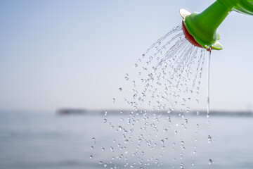 Close Up of a toy watering can pouring a shower of water on the beach. Fun with children on the beach © DinoPh