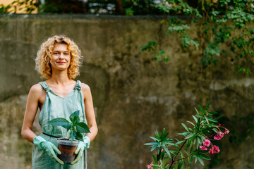 Portrait of positive charming female gardener wear mint gloves caressing blooming oleander tree in...