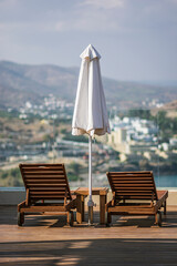 Two sun lounger beds next to a closed sun shade parasol umbrella on wooden decking. © Stephen