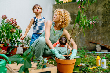 Cute child boy hugging his mother gardener at backyard garden. Happy lovely mom with children outdoor. Hobbies and leisure, home gardening, houseplant, urban jungle concept.