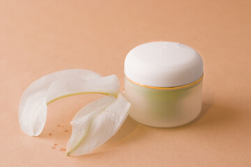 Cosmetics concept. Round jar for cream on a brown background next to the petals of a white flower