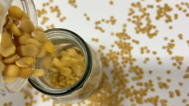 Organic yellow Split Pigeon Peas flowing into a glass container on a white background