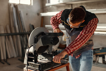 Young man work in home workshop garage with a grinder cuts metal bar