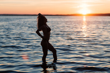 Caucasian fit woman with sport body is posing on beach at sunset time.