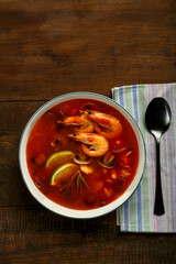 Tom yam soup with shrimp and lime in a light plate next to a spoon on a napkin.