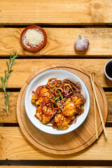 Soby with chicken and sesame seeds in teriyaki sauce on a wooden stand and sticks next to sesame seeds, herbs and soy sauce on a wooden table.