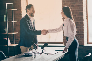 Profile photo of two people businessman business lady partnership doctors colleagues press conference mass media shake arms greeting reportage microphone on table office indoors